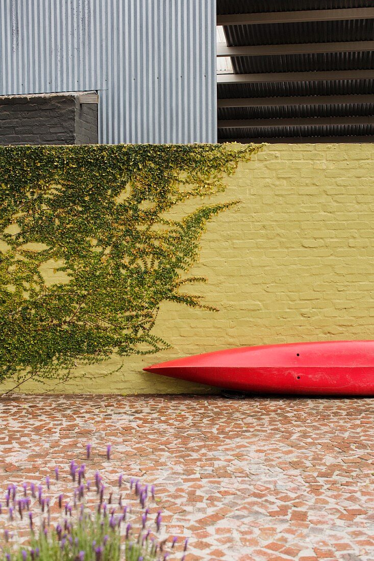 Ein rotes Kanu lehnt an einer gelben Backsteinwand im Hof