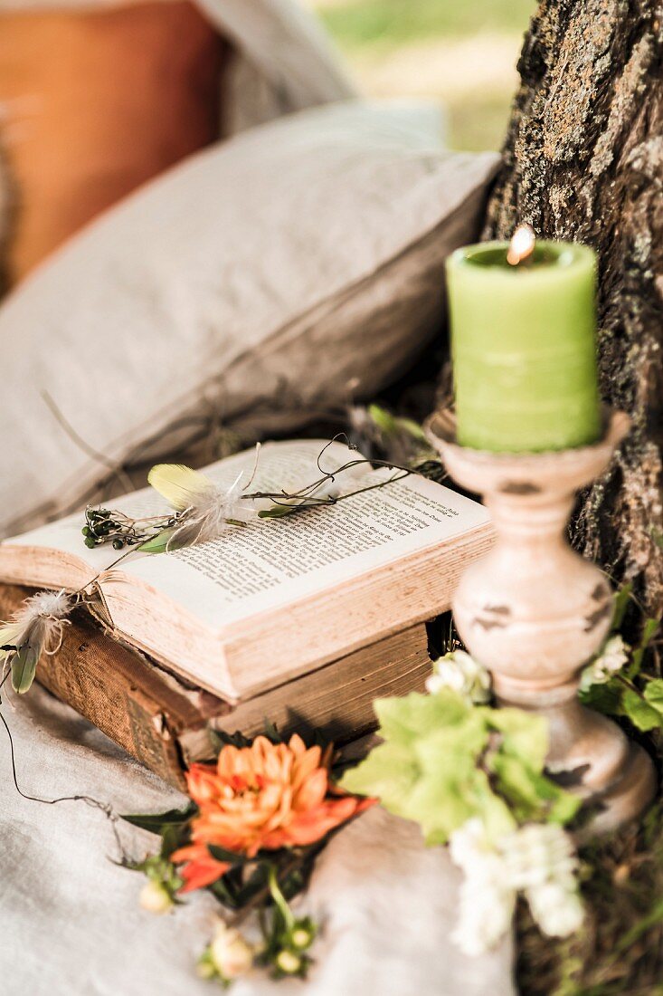 Romantic seating area with candle and flowers next to open book on tree trunk