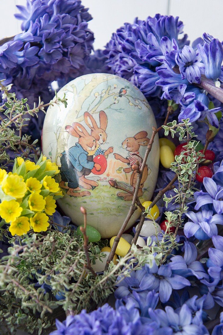 Hollow paper Easter egg in next of hyacinths, cowslips, thyme and sugar eggs