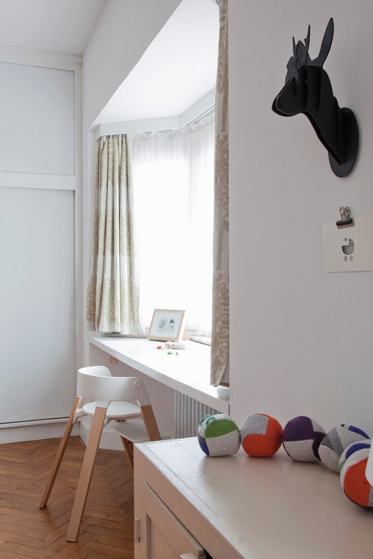 Stylised black hunting trophy above fabric balls on cabinet and white high stool next to windowsill