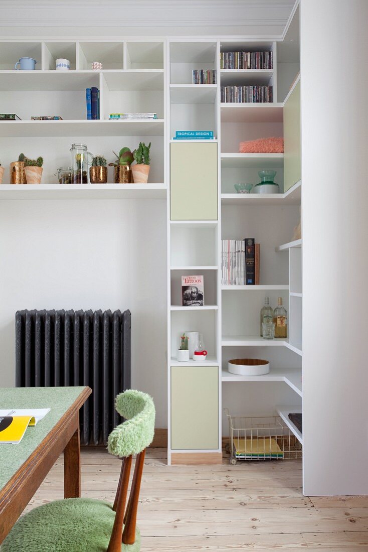Custom-made, white shelves with open compartments and cupboards behind retro wooden chair