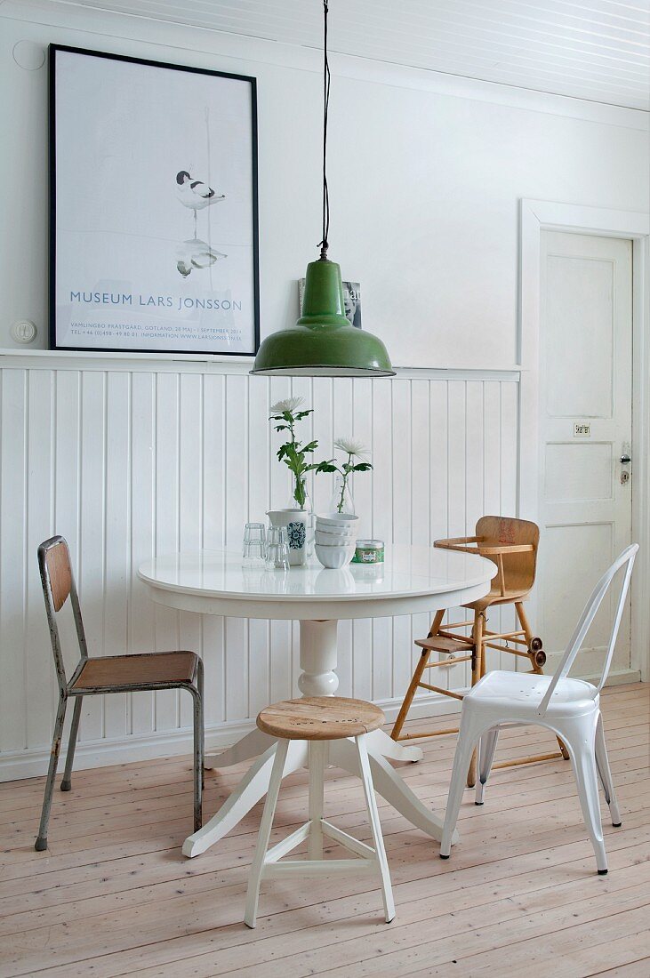 Runder Tisch mit verschiedenen Stühlen vor Wand mit Bretterverkleidung