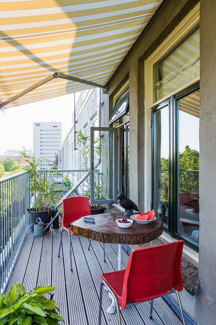 Yellow awning, wooden table and red chairs on urban balcony