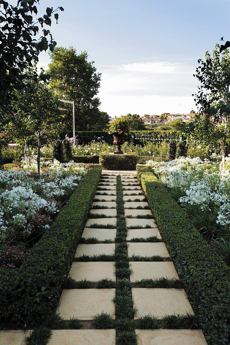 Geometrisch angelegter Garten mit gepflegter Buchshecke, weiß blühendem Agapanthus und Rondell mit bepflanzter Amphore