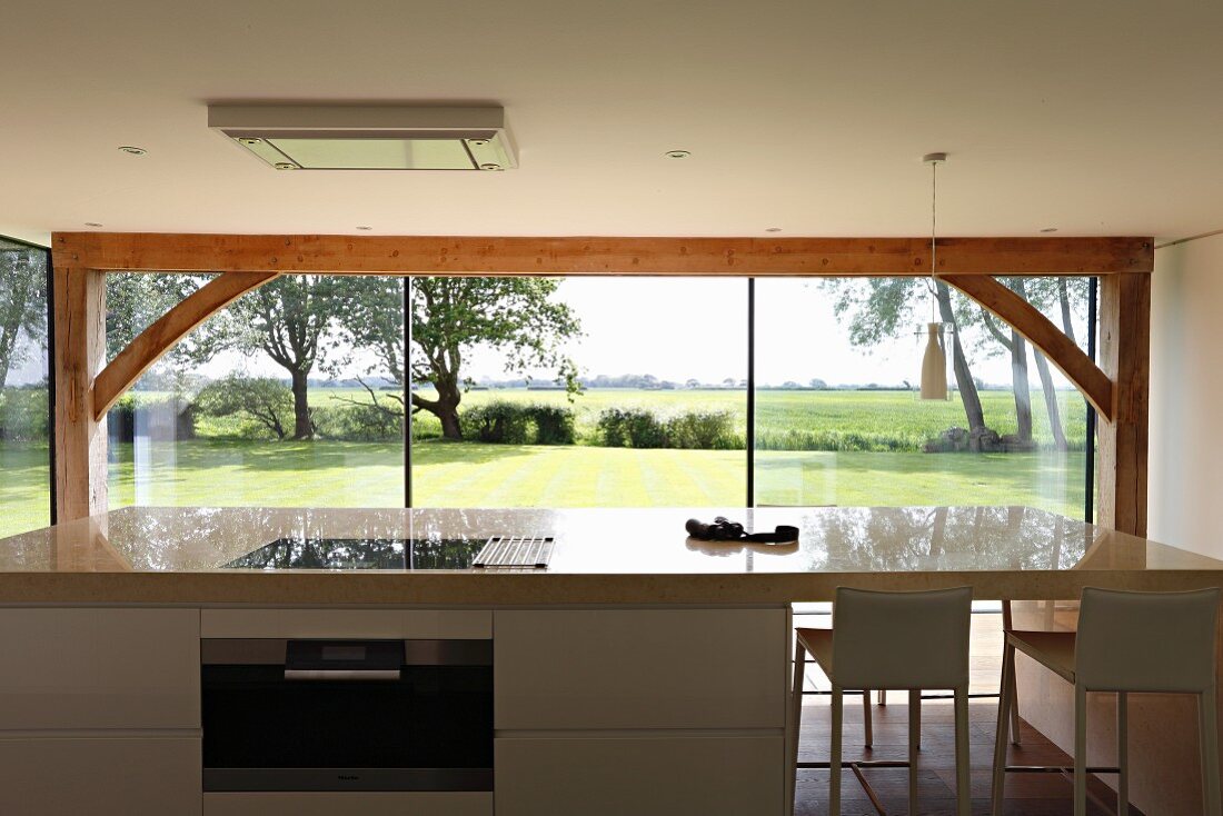 View across free-standing kitchen counter through panoramic window to green landscape