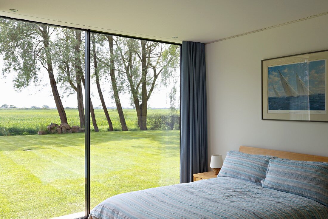 Modern bedroom with glass wall overlooking sunny lawn