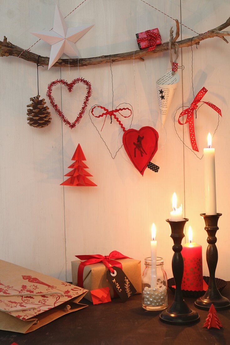Weihnachtsdeko an rustikalem Ast hängend, darunter Kerzenhalter mit brennenden Kerzen
