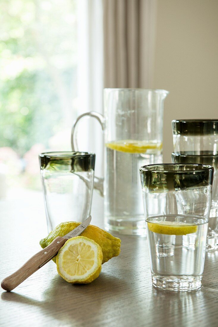 Lemons, glass of water and jug of water on table