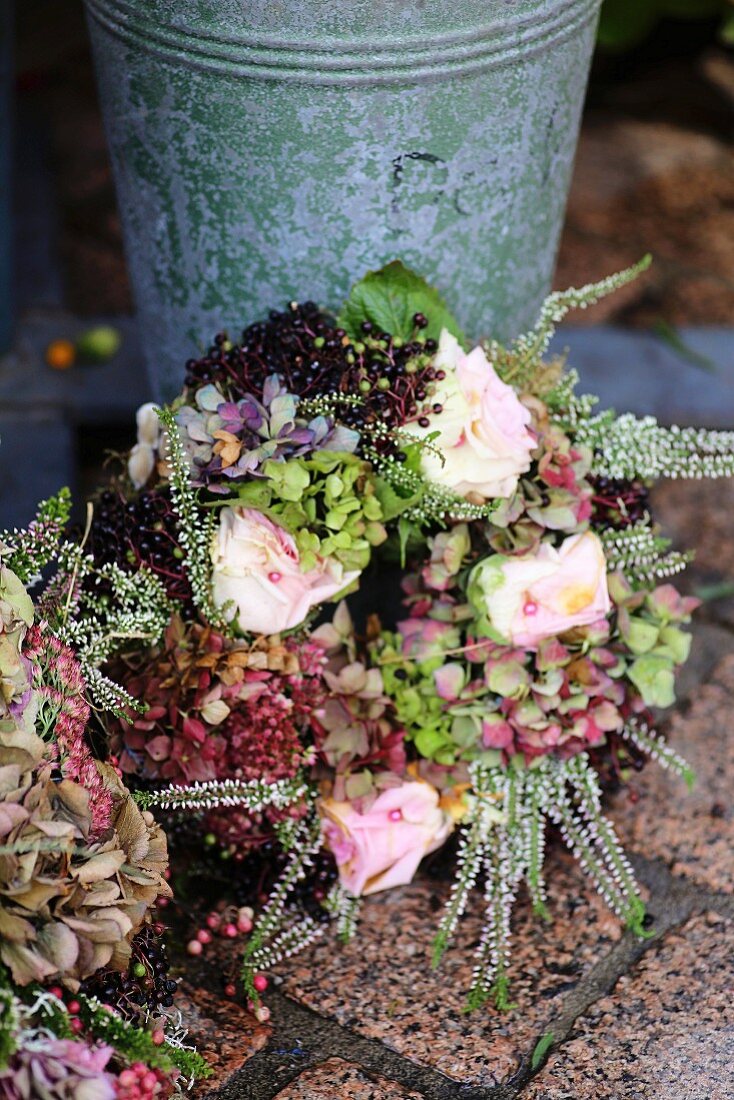 Herbstilicher Kranz aus getrockneten Hortensien, Rosen, Holunderbeeren und Erika an Zinkgefäss