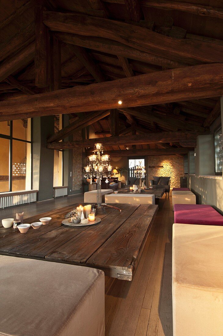 Wohnraum mit sichtbarem Dachstuhl aus Holz, Polsterbänke und Couchtisch mit Platte aus Holzbrettern