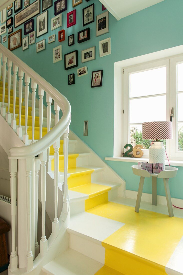 Weiß lackierte Holztreppe mit gelbem Farbstreifen in türkisgrün gestrichenem Treppenhaus mit Fotogalerie