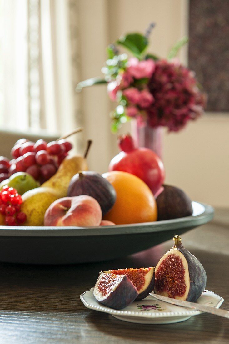 Aufgeschnittene Feigen auf Teller und grosse Obstschale mit verschiedenen Früchten