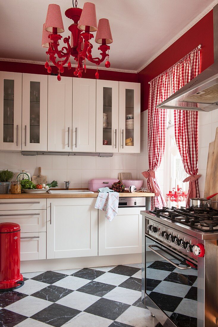 Schachbrettfliesen, rot-weiss karierte Vorhänge und poppiger Kronleuchter in weisser Küche
