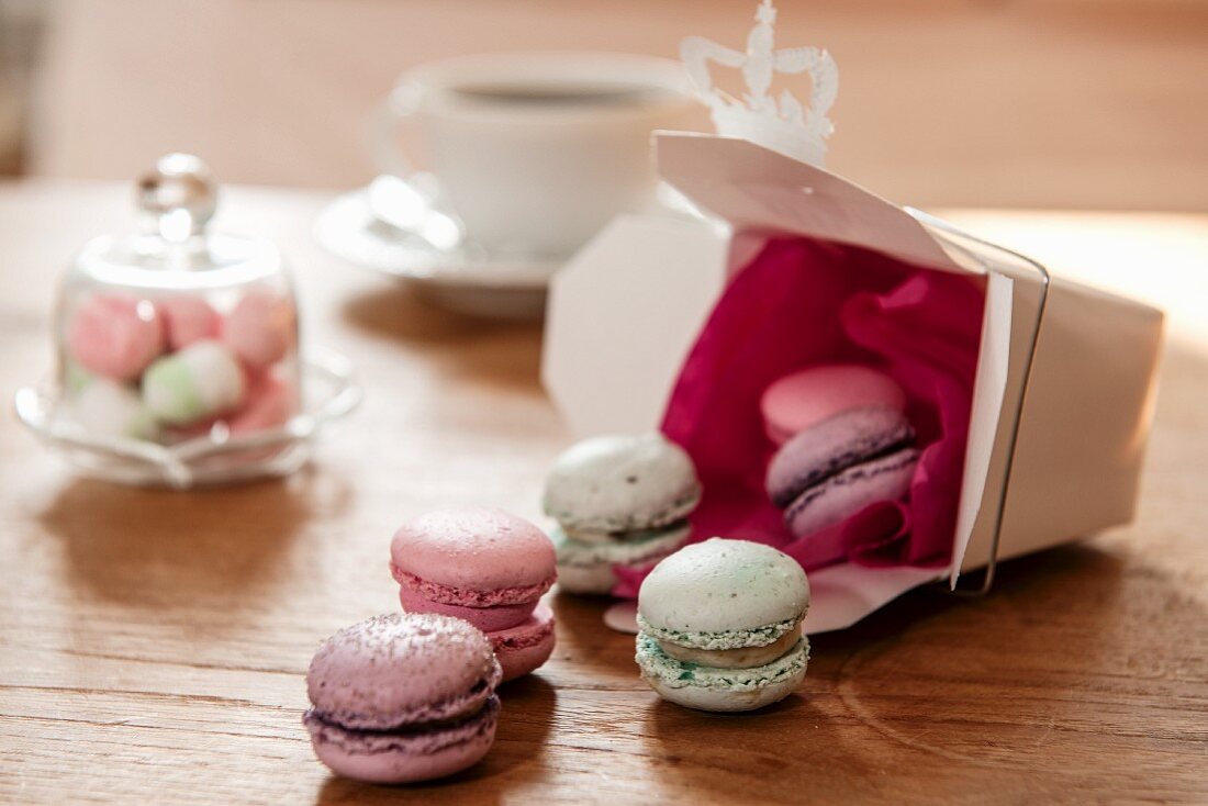 Colourful macarons tumbling onto wooden table from gift box