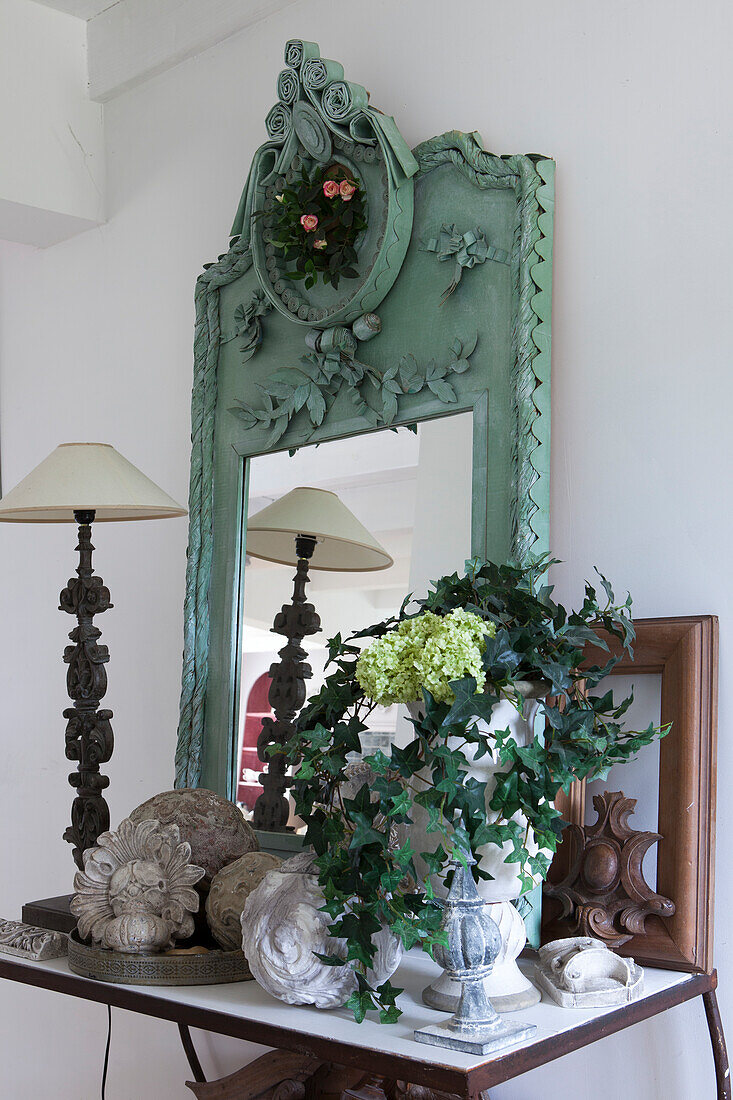 Potted plant, table lamp and mirror with turquoise frame arranged on console table