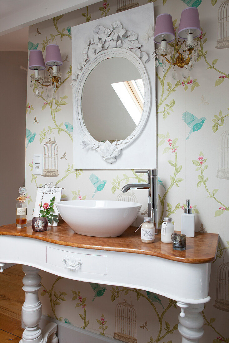 Countertop basin on washstand below mirror in ornate frame on patterned wallpaper