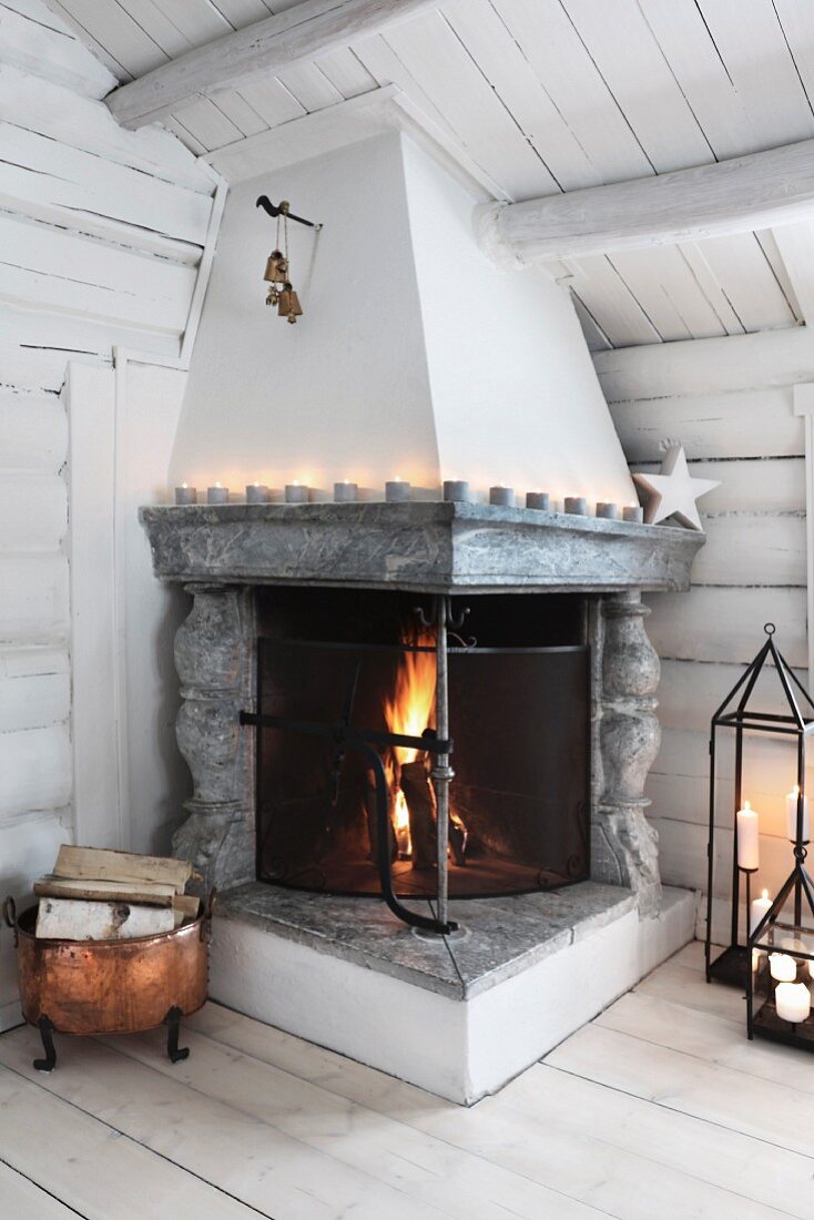 Offener Kamin mit brennendem Feuer und Kerzendeko in einer Blockhütte