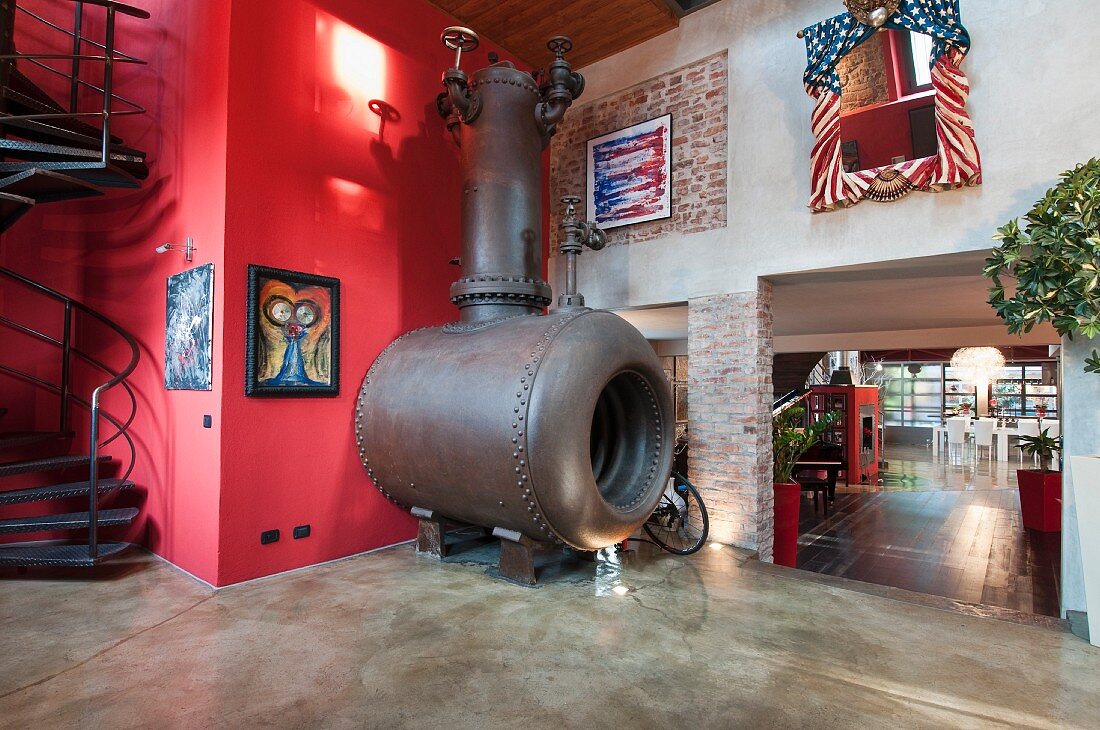 Enormous old industrial stove against bright red wall in loft apartment with stairs leading to gallery