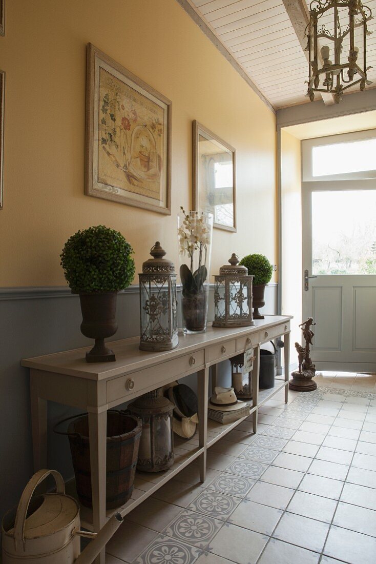 Lanterns and small bushes decorating console table in rustic hallway