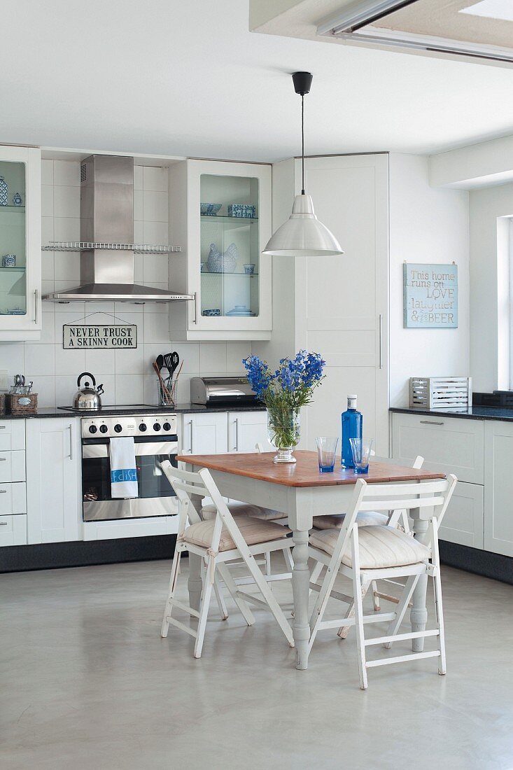 Kleiner Essplatz mit Klappstühlen in moderner Einbauküche, blaue Akzente durch Blumenstrauss und Flasche auf dem Tisch