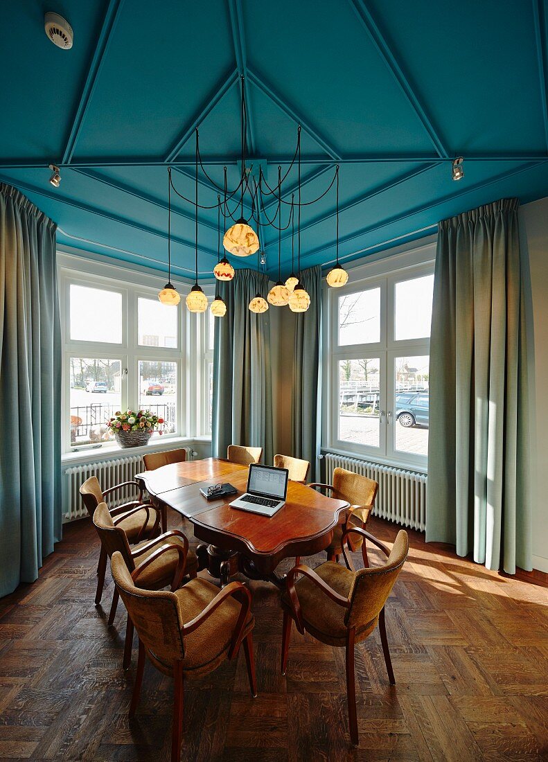 Antique table and chairs below blue-painted ceiling with multiple pendant lamps in meeting room
