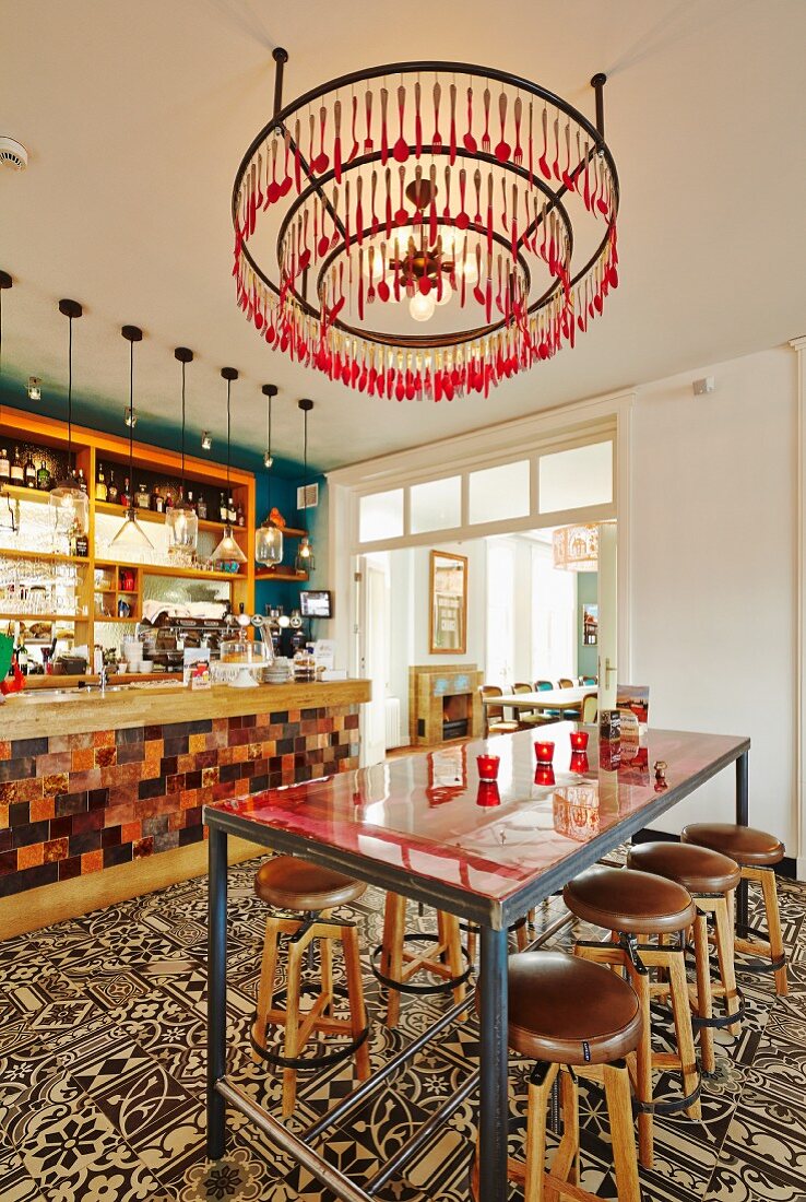 Minimalist counter and bar stools on tiled floor with vintage ornamental pattern in bar; chandelier made from concentric metal rings and cutlery painted pink