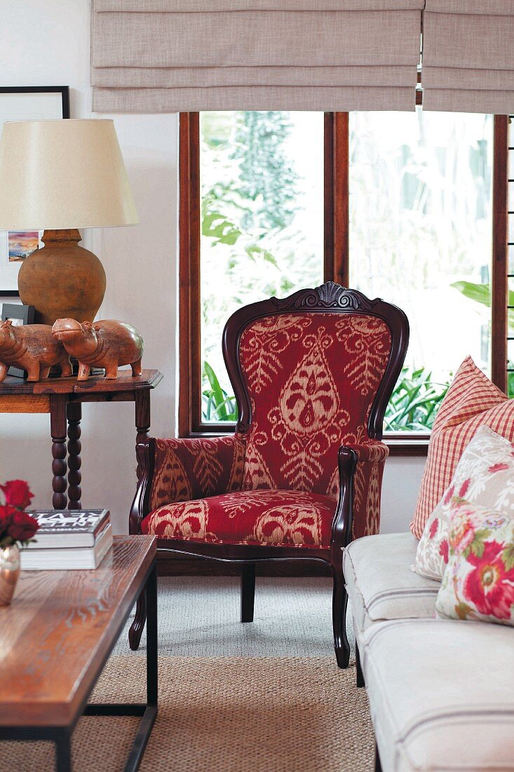 Antiker Sessel mit dekorativem Bezug, davor ein Sofa mit floralen Kissen und Couchtisch