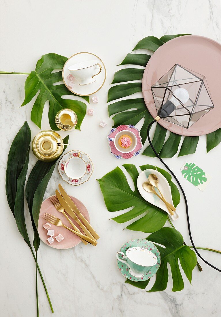 Tischdekoration mit grünen Pflanzenblättern, nostalgischen romantischen Kaffeetassen und Goldbesteck auf marmorierter Tischplatte