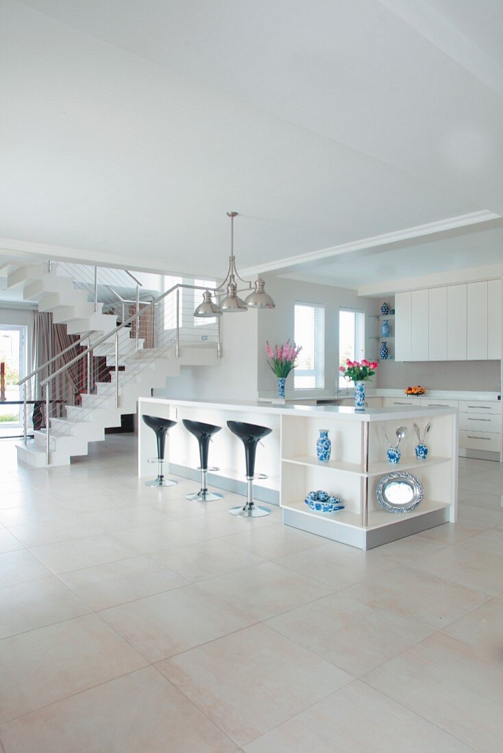 Designer kitchen in open-plan white interior with black 'Bombo' bar stools at elegant island counter