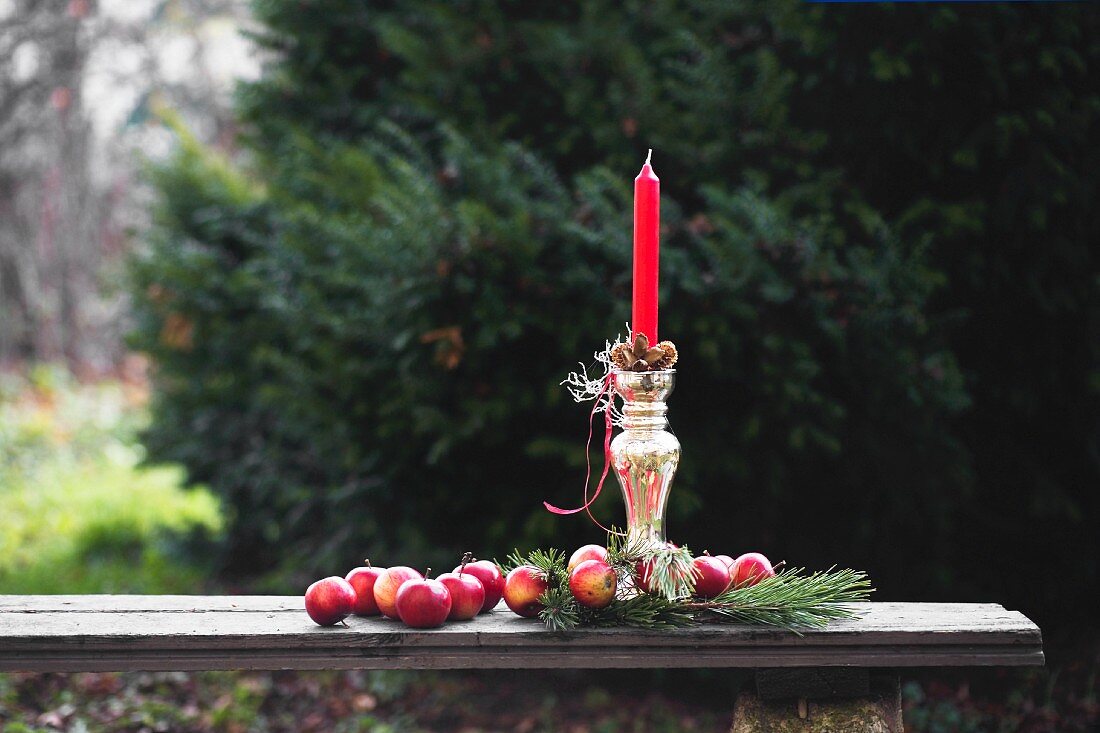 Red apples and pine cones around red candle in silver candlestick