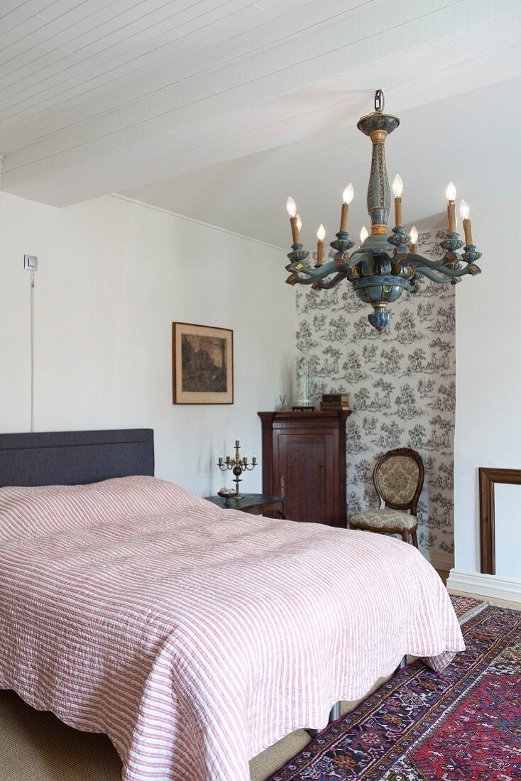 Doppelbett mit gestreifter Tagesdecke, an weisser Holzdecke nostalgischer Kronleuchter in ländlich traditionellem Schlafzimmer