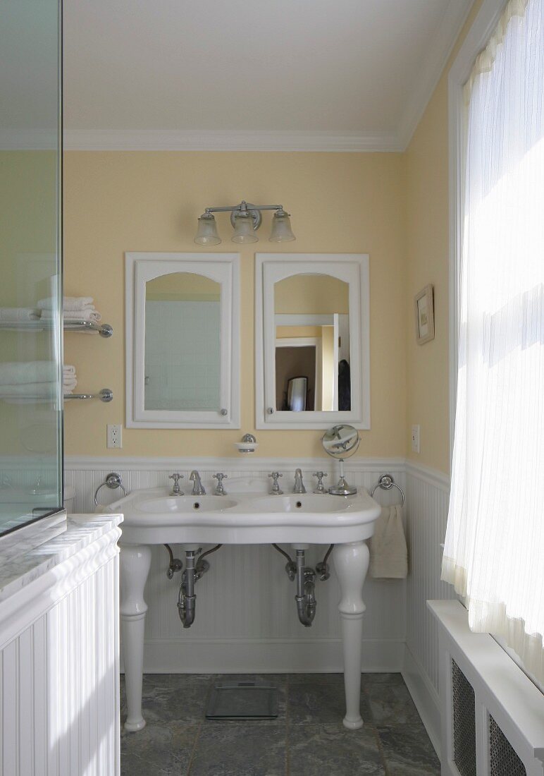 Blick in traditionelles Bad auf Vintage Standwaschbecken vor pastellgelber Wand, eingebaute Schränkchen mit Spiegeltür