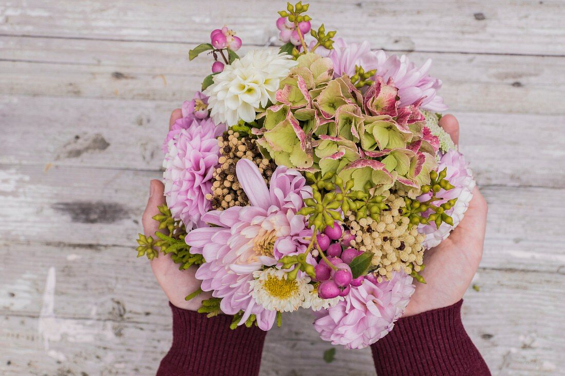 Hände halten Blumengesteck aus Chrysanthemen, Dahlien und Hortensie