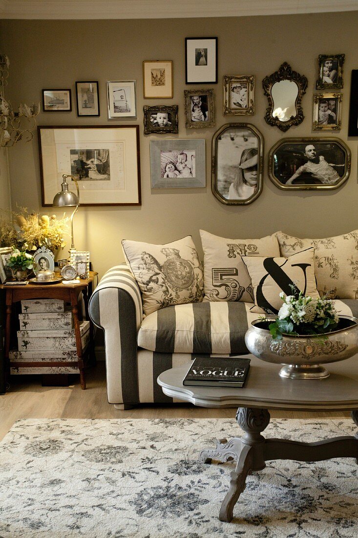 Wohnzimmer mit nostalgischem Flair; Couch mit Streifenbezug und Kissen vor hellgrauer Wand mit Fotogalerie
