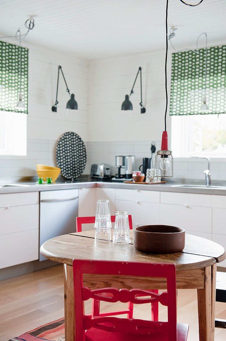 Runder Holztisch und rote Stühle in Küche mit weissen Unterschränken