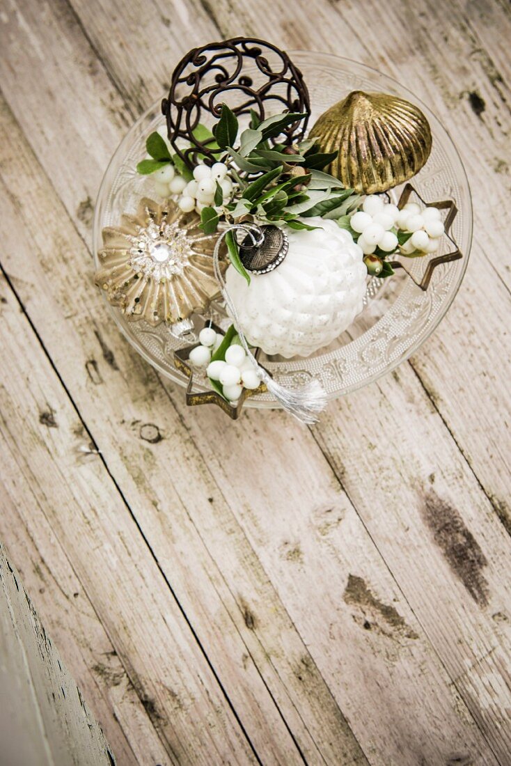 Glasschale mit Vintage Weihnachtsschmuck und Schneebeeren auf Holztisch