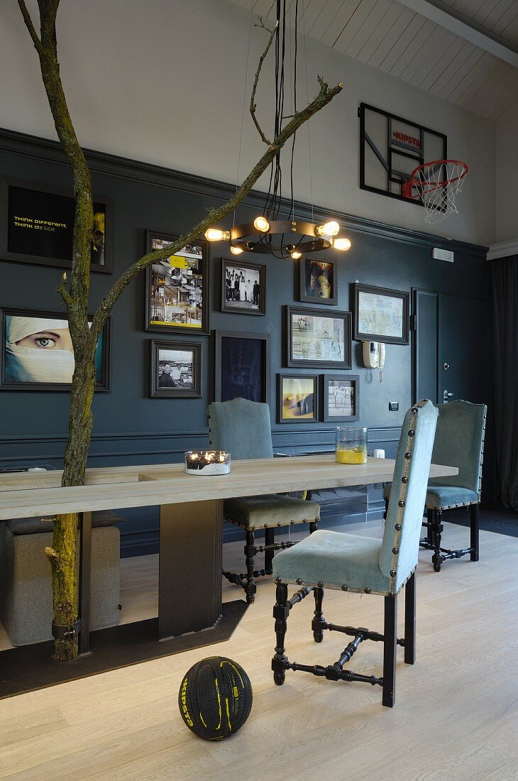 Massgefertiger Holztisch mit Metall Untergestell und gepolsterte Vintage Stühle, im Hintergrund Bildersammlung und Basketballkorb an Wand