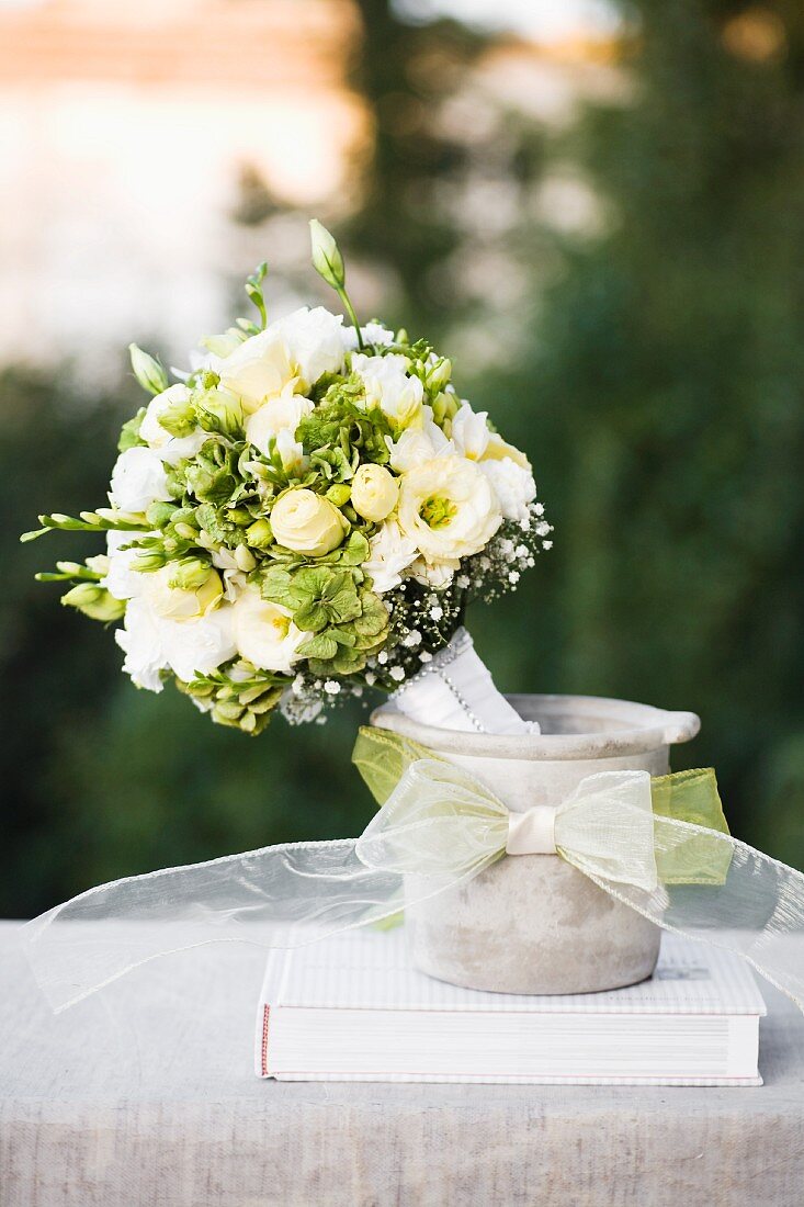 Festlicher Blumenstrauss mit weissen Blumen in Pflanzgefäss aus Beton verziert mit Schleife