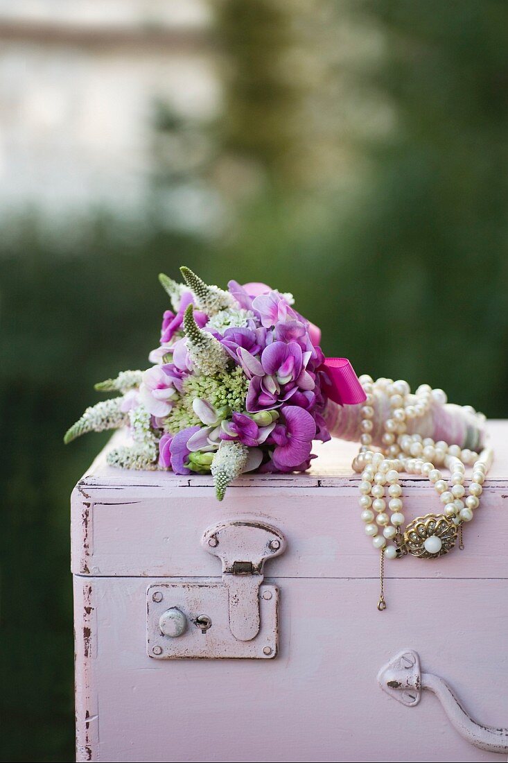 Festlicher Blumenstrauss mit Perlenkette verziert, auf Holztruhe pastellfarben lackiert