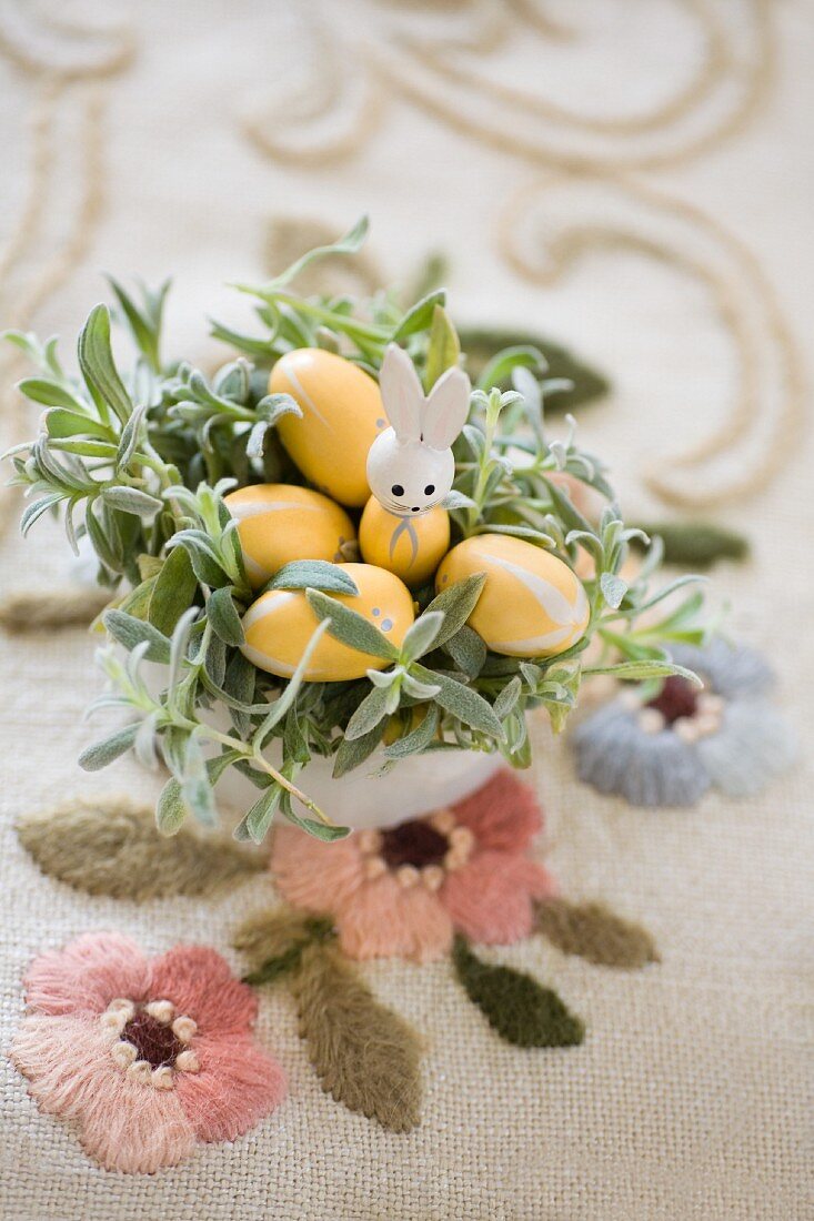 Easter nest made from planted pot with rabbit ornament and wooden eggs on embroidered vintage tablecloth