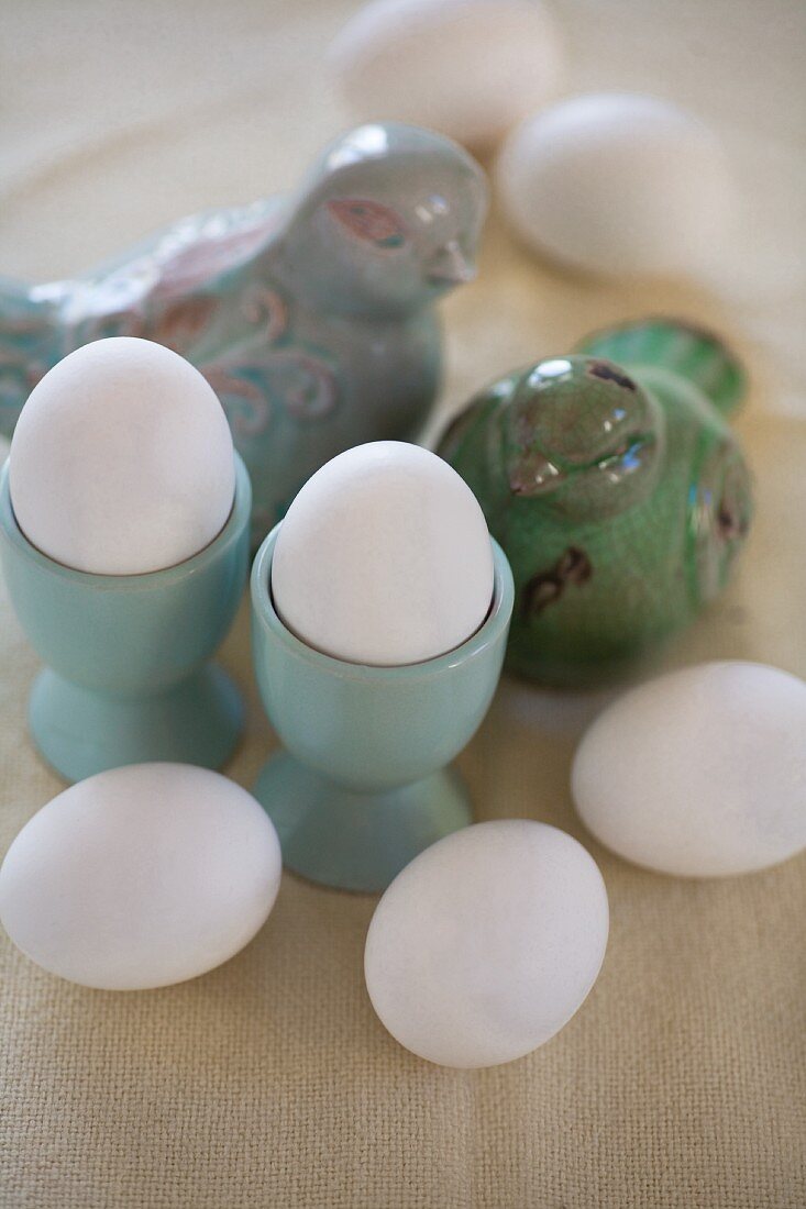 weiße Eier in türkisfarbenen Eierbechern und Vogelfiguren