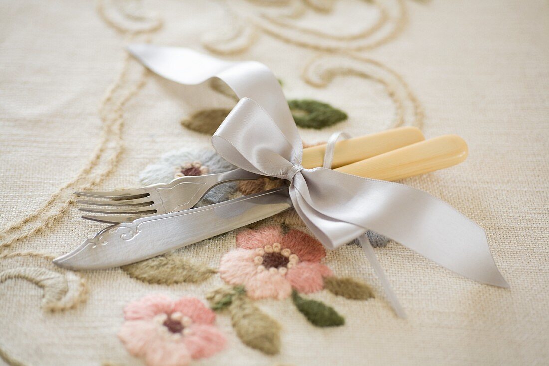 Vintage cutlery with cream plastic handles tied with ribbon on embroidered tablecloth