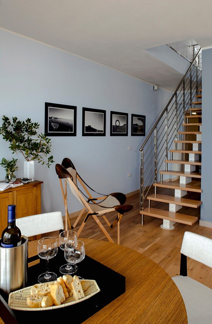 Essbereich, Hintergrund Sessel im Klassikerstil vor Treppenaufgang, in hellblau getöntem Wohnraum