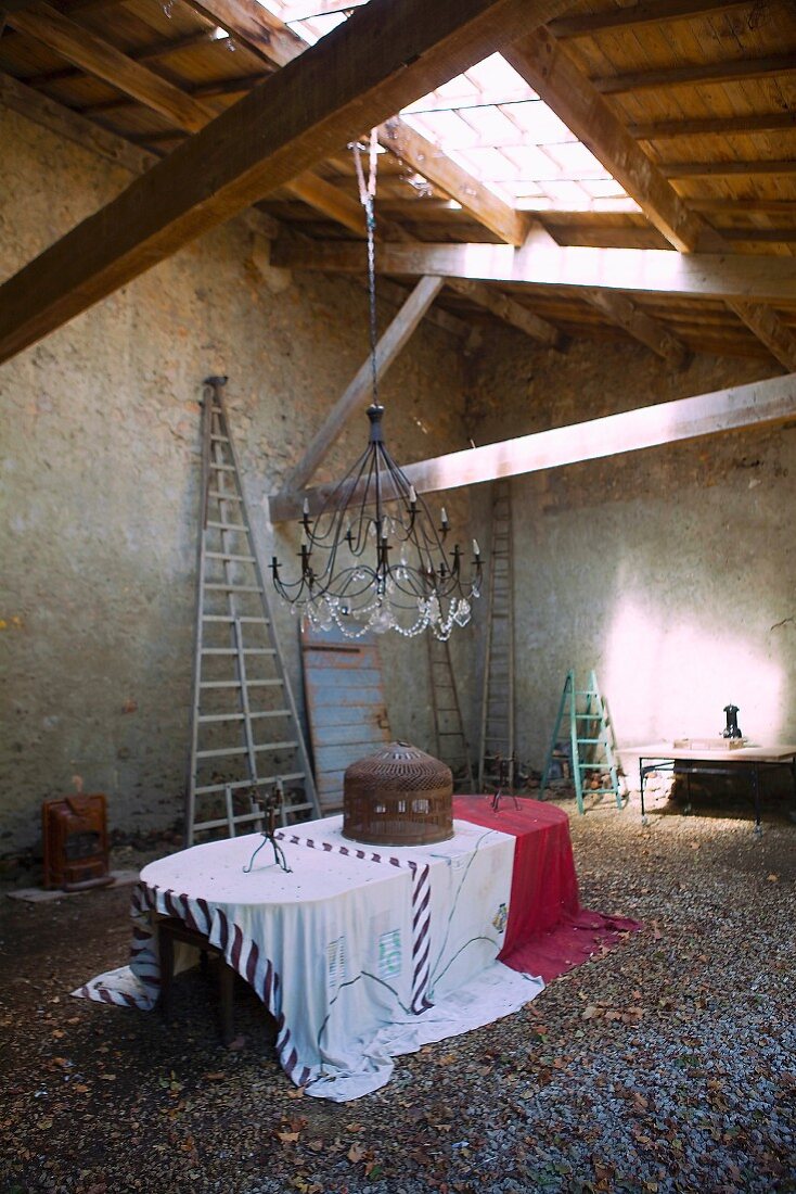 Tisch mit Tischdecken unter Kronleuchter, an Holzdecke mit Oberlicht in alter Scheune