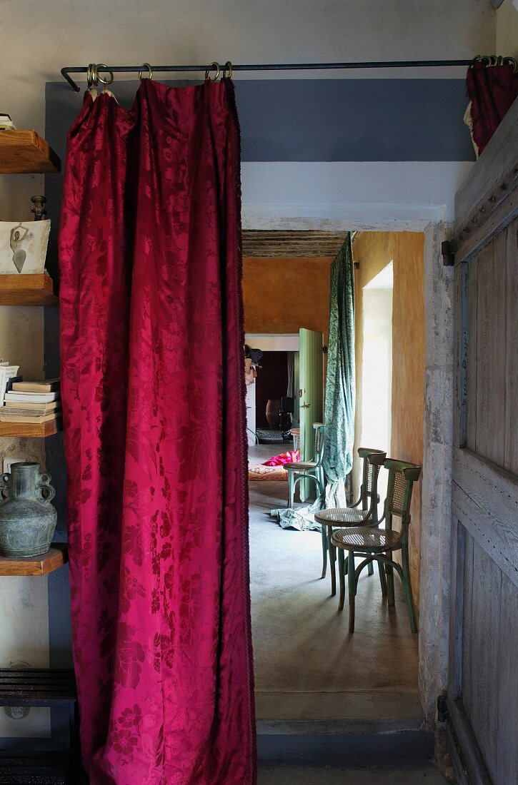 Red brocade curtain hanging in doorway with view of vintage wooden chair against yellow-painted wall