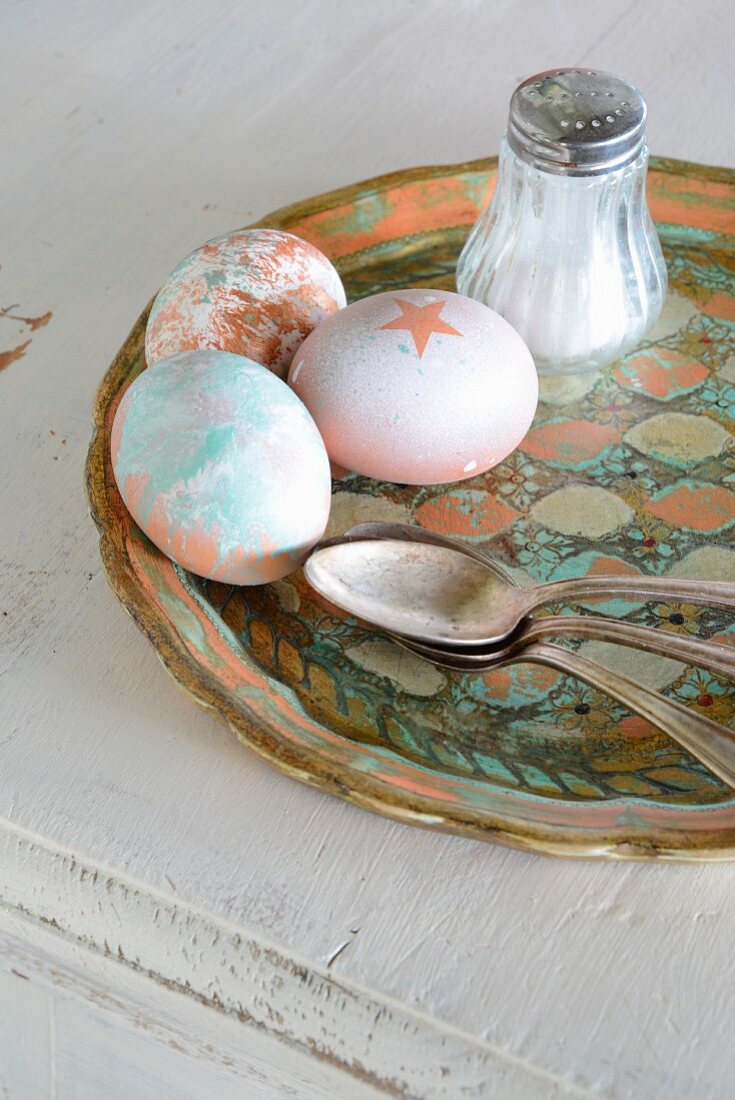 Variously painted Easter eggs, silver spoon and salt cellar on vintage tray