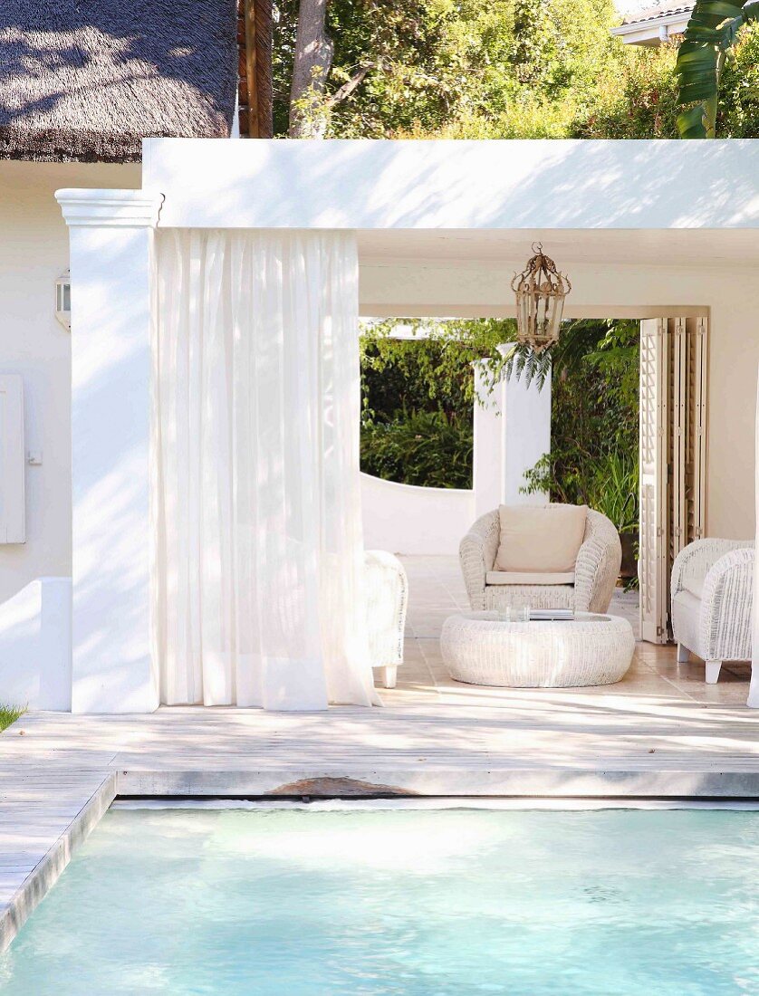 Eleganter sommerlicher Loungebereich am Pool mit weißen Korbmöbeln