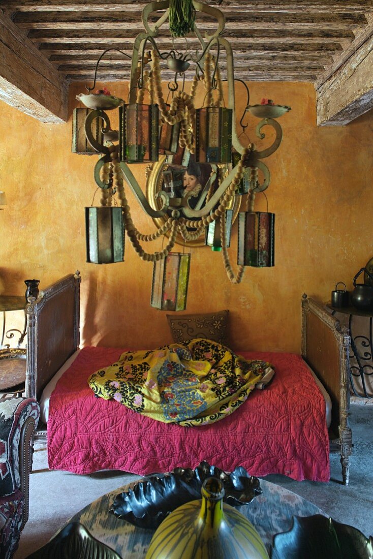 Vintage Schlittenbett vor goldgelb getönter Wand, im Vordergrund Pendelleuchte mit aufgehängten Windlicht-Laternen