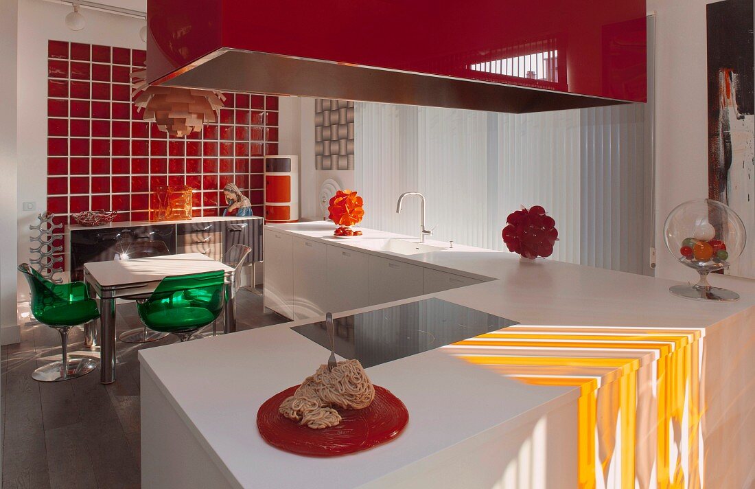 weiße Küchenzeile und roter Dunstabzugshaube in offenem Kochbereich, Essplatz vor orangeroter Glasfliesenwand im Hintergrund