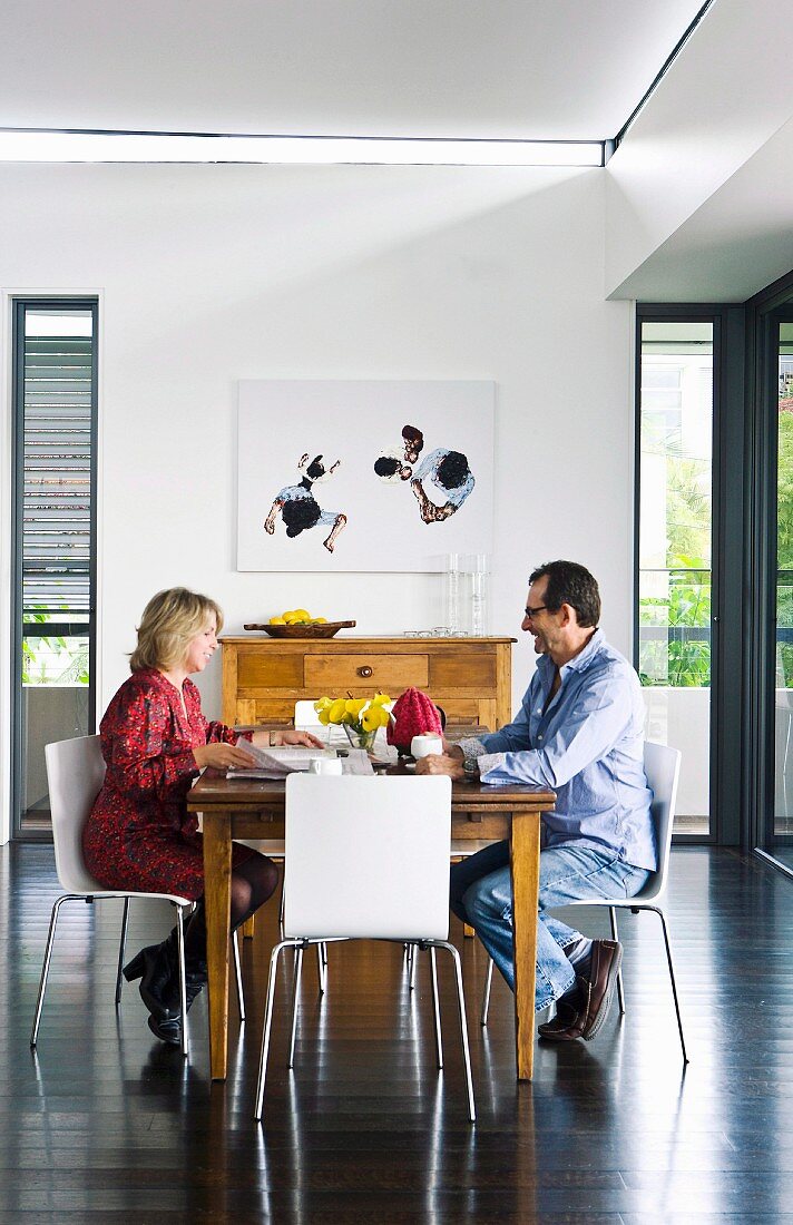 Mann und Frau am Frühstückstisch, moderne, weiße Stühle um Esstisch aus Holz in zeitgenössischem Ambiente